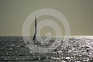 Small sailboat sailing on calm sea at sunset