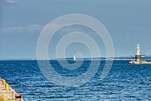 A small sailing boat in Aarhus harbour sails in a calm sea beside Arhus Lighthouse inspiring a romantic escape or a sport activity