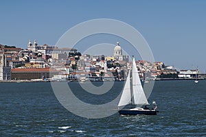 Small sailing boat in the Tagus River with the Lisbon skyline on the background