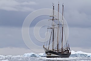 Small sailing ship in Antarctic waters between ice floes and ice