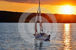 A small sailing ship sailing on a calm sea at the sunset