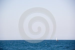 Small sailing yacht with big white sails in the open sea on the horizon