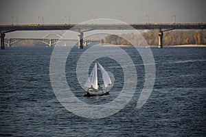 A small sailing yacht floats along the river, and in the background are two long bridges