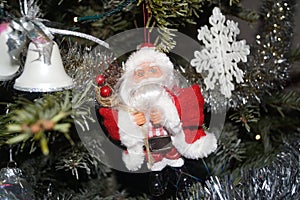 A small Santa Claus was hung on in the fir tree, on one side there are small bells and on the other side flake of Christmas. Front