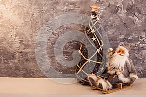 Small Santa sitting on a sled near wicker Christmas tree