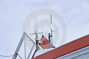 Small satellite dish antenna ?n rooftop behind building dark cloudy sky is background.