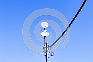 Small satellite dish antenna with wires blue sky, bright sunlight in background.