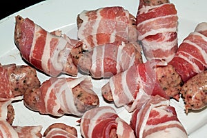 Small sausages, pigs in blankets, wrapped in bacon strips ready to cook.