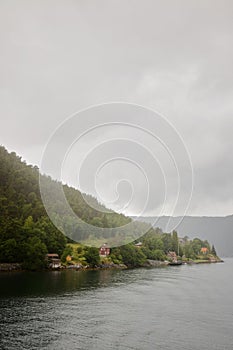 Small Scandinavian houses stand on the shore of the fjord on a rainy cloudy day