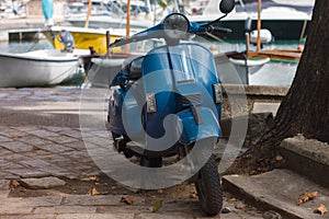 Small scooter in blue parked by a tree on the pier