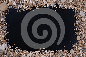 Small sea stones and shells, on a black background, with a free space under the text, title, ad, menu or picture.