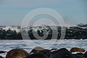 Small sea waves break against the stones of the shore. A bright sunny day and white foam of the waves. Melting glaciers