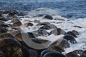 Small sea waves break against the stones of the shore. A bright sunny day and white foam of the waves. Melting glaciers