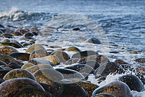 Small sea waves break against the stones of the shore. A bright sunny day and white foam of the waves. Melting glaciers