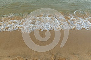 Small sea waves breaking on sandy beach in soft sunset light