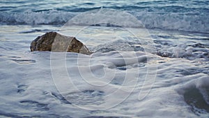 Small sea waves at shore washing rock on sandy beach, closeup morning detail