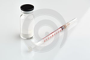 Small sealed bottle with medicine and syringe on white background