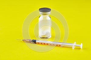 Small sealed bottle with medicine and syringe on yellow background