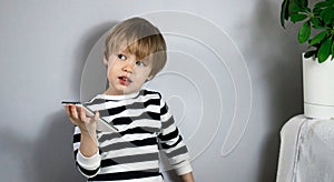 A small serious blond European European boy holds a mobile phone smartphone and looks towards the free space