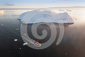 Small ship cruising among ice bergs during beautiful summer day. Disko Bay, Greenland.