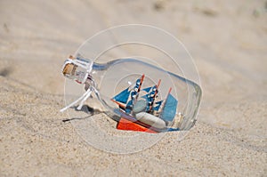 Small ship in the glass bottle lying in the sand