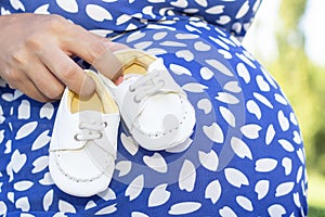 Small shoes for the unborn baby in the belly of a pregnant woman.
