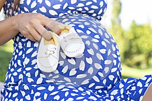 Small shoes for the unborn baby in the belly of a pregnant woman.