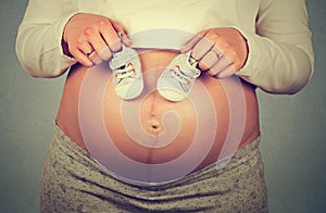 Small shoes for the unborn baby on the belly of pregnant woman