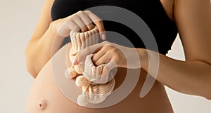 Small shoes for the unborn baby in the belly of pregnant woman. Close up. Motherhood, pregnancy, people and