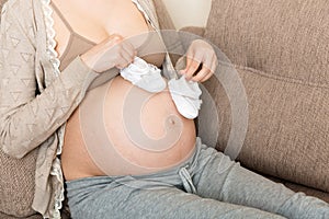 Small shoes for the unborn baby in the belly of pregnant woman ion sofa at the house