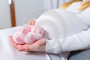 Small shoes for the unborn baby in the belly of pregnant woman. Pregnant woman holding small baby shoes relaxing at home in