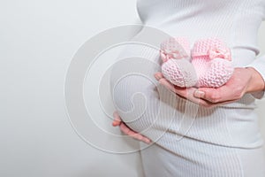 Small shoes for the unborn baby in the belly of pregnant woman. Pregnant woman holding small baby shoes relaxing at home in