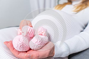 Small shoes for the unborn baby in the belly of pregnant woman. Pregnant woman holding small baby shoes relaxing at home in