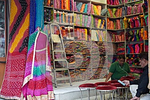 Small shop owner indian man selling shawls, clothing and souvenirs at his store. Colorful traditional Indian costume/outfit for