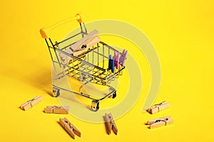 Small shopping cart with clothes pins on color background
