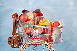 Small shopping cart with different pet goods and Christmas gifts on light blue background. Shop assortment