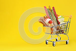 Small shopping cart with different pet goods on yellow background, space for text. Shop assortment