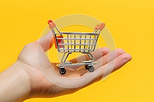 Small shopping cart in female hand on yellow background. Shopping concept. Ai generative