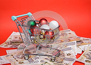 Small shopping cart full of balls from Christmas tree stands on lot of banknotes