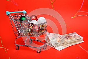 Small shopping cart full of balls from Christmas tree stands on lot of banknotes