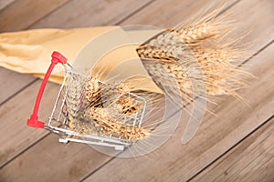 A small shopping cart full of ripe wheat ears and a handful of wheat ears next to it