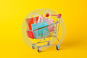Small shopping cart with paper bags on yellow background