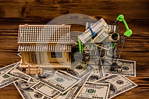 Small shopping cart with rolled up one hundred dollar banknotes and plywood model of the house on a wooden background. Loan, real