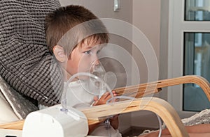 Small sick boy with nebulizer mask making inhalation, respiratory procedure by pneumonia or cough for child in home. Treatment at