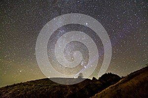 Small silhouette of man with flashlight on green grassy hill under dark blue summer starry sky.