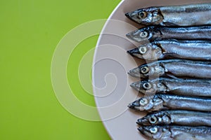 Small silver fish in a beige plate on a wooden table, close up