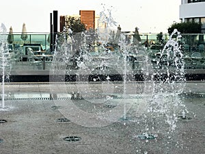 A small singing fountain in the open air, on the street. Drops of water, jets of water frozen in the air in flight