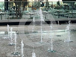 A small singing fountain in the open air, on the street. Drops of water, jets of water frozen in the air in flight