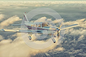 Small single engine airplane flying in the gorgeous sunset sky through the sea of clouds above the spectacular mountains photo