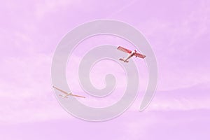 Small single-engine old vintage plane and glider flying against the pink sky, concept of teamwork, dream, happy future and